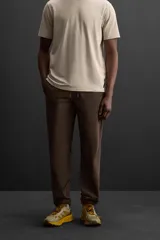 Pantalón deportivo color marrón oscuro, corte regular fit, confeccionado en tejido técnico ligero y elástico. Cuenta con cintura elástica ajustable con cordón, bolsillos frontales con cierre de cremallera, bolsillo trasero con cierre de cremallera oculta en costura y bajo ajustable con elástico.