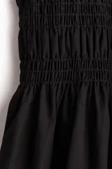 Vestido corto negro de popelina de algodón con escote cuadrado y mangas cortas abullonadas con elástico. El cuerpo es ajustado con fruncido y la falda con vuelo. Tiene ribete de volado en escote y puños.