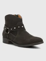 Bota corta de mujer color gris oscuro o marrón oscuro, estilo botín biker, confeccionada en gamuza. Presenta una tira decorativa con tachas metálicas plateadas y hebilla. Tiene un taco bajo y punta ligeramente afilada.