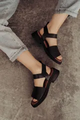 Sandalias bajas color arena, con tiras anchas de cuero y hebilla lateral.