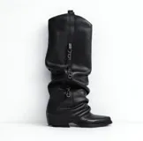 Bota alta de cuero negro con caña arrugada y detalles de cadenas colgantes.