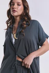 Camisola verde grisáceo de tencel con cuello camisero, mangas cortas con dobladillo y cierre frontal con botones.
