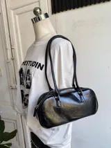 Cartera tipo baguette de cuero sintético negro con cierre superior y correa de hombro fina.
