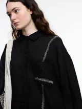 Camisa de manga larga de lino color azul con calce relajado y diseño asimétrico. El bolsillo delantero está colocado de forma invertida, un detalle lúdico que rompe con lo clásico. Lleva un bordado tipo pespunte en color contraste que recorre el frente y el bolsillo.