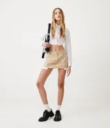 Minifalda color beige de sarga con cintura baja, trabillas, cierre con corchete y cremallera, y forro de bolsillo aparente.