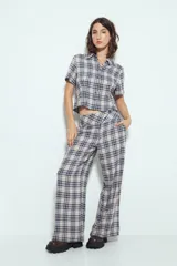 Pantalón de vestir de pierna amplia y tiro alto, con estampado de cuadros escoceses en tonos azul marino, beige y blanco. Presenta un cruce frontal con un botón visible.