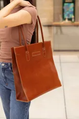 Bolso tote de cuero color marrón, con costuras a contratono y logo grabado en el frente.