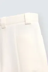 Pantalón color crema de corte ancho, con pliegues frontales, bolsillos laterales y traseros.