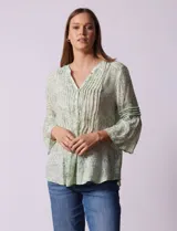 Blusa de gasa estampada con flores, color verde claro. Cuello a la base, escote en V y abertura central con botones. Delantera con plisados y mangas 3/4 con terminación amplia.