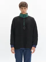 Buzo de sherpa color negro con cuello alto, cierre frontal y detalles bordados.