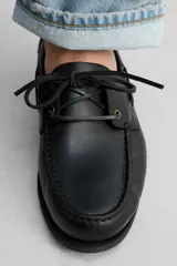 Zapato náutico de cuero negro con cordones de cuero y suela plana.