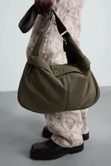 Bolso de hombro color verde oliva, fabricado en tejido técnico acolchado. Tiene un compartimento principal con cierre de cremallera, un bolsillo interior con cremallera y un bolsillo frontal con cremallera. El asa de hombro es ajustable.