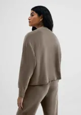 Buzo color beige en tela acanalada con cuello alto y puños ajustados.