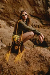 Bolso bandolera marrón de gamuza con flecos amarillos. Tiene un bordado en forma de sol en el frente.
