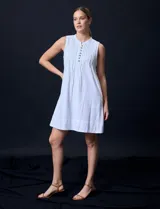 Vestido corto blanco de algodón y rayón, sin mangas, con cuello a la base, abertura central con botones y detalle plisado en la delantera. Incluye bolsillos laterales.