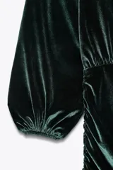 Vestido corto de terciopelo verde esmeralda, con escote fluido, mangas largas abullonadas y aberturas en los hombros.