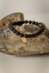 Pulsera elástica de piedras naturales color marrón con dije circular dorado con la palabra "AIRE" grabada.