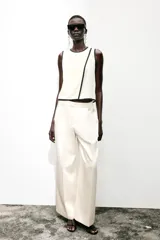 Blusa blanca sin mangas de crepe con cuello redondo y detalle de ribete negro en cuello, sisas y abertura frontal diagonal.