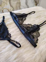 Conjunto de lencería negro de encaje, compuesto por un bralette con breteles regulables y una tanga regulable con corte cola less y entrepierna de algodón.