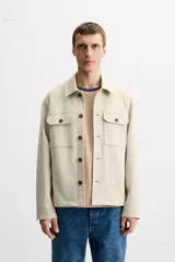 Sobrecamisa color beige de corte recto, con cuello solapa, manga larga con puños abotonados, cierre frontal abotonado, bolsillos de parche con solapa en el pecho y bolsillos de ojal en la cadera.
