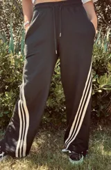 Pantalón de jogging color gris claro, corte ancho, con cordón ajustable en la cintura y tres rayas negras verticales en los laterales.