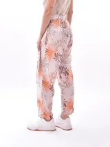Pantalón babucha de tela estampada con hojas en tonos rosa, naranja y azul, con cintura elastizada y lazo para ajustar.