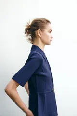 Chaqueta azul marino de punto con cuello solapa y manga corta. Incluye cinturón fino con hebilla dorada y cierre frontal con botones a tono.