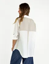 Camisa beige de lino con mangas 3/4, cuello camisero, cierre con botones y detalle de bolsillo en el pecho. Presenta una tira vertical en color marrón a lo largo del frente.