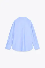 Camisa celeste de popelina de algodón, con cuello solapa, escote pico, manga larga con puños y cierre frontal con botones.