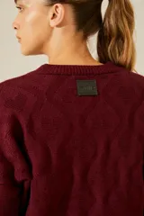 Sweater color borgoña de punto con cuello redondo, diseño de rombos con tachas aplicadas y detalle de corazones de cuero en la espalda.