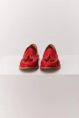 Mocasín de cuero color marrón claro, con detalle de flecos y borlas en la parte delantera. Diseñado en Uruguay y fabricado en Brasil.
