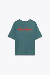 Camiseta de manga corta color verde azulado (teal) con efecto lavado, corte oversize y cuello redondo. Estampado frontal en color rojo con el texto "Sapore Felice" en tipografía cursiva.