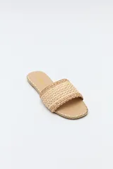 Sandalias planas color beige, con capellada ancha de tejido trenzado con texturas naturales y detalles de hilo contrastante.