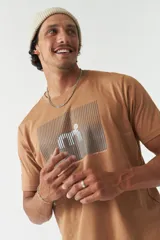 Remera color marrón con estampado rectangular con líneas horizontales y figura geométrica en el centro.