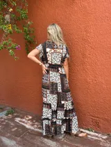 Vestido largo con estampado tipo patchwork en tonos tierra, blanco y azul oscuro. Presenta escote cruzado en V y mangas cortas. La falda es larga y con vuelo.