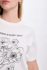 Remera blanca de algodón con cuello redondo y mangas cortas. Estampa de flores y texto en color negro.