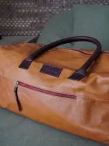 Bolso de viaje tipo weekender de cuero color marrón, con doble asa corta y correa larga desmontable. Cuenta con cierre superior, bolsillos internos y externos con cierre metálico. Forro interior de tela. Marca Sierra Mora.