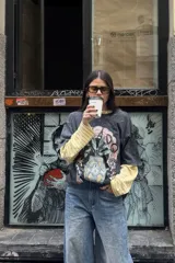 Remera de manga corta, color gris oscuro con efecto lavado, con un estampado frontal que incluye un diseño de planta en una maceta decorada, serpientes y texto. Se usa superpuesta a una remera de manga larga a rayas amarillas y blancas.