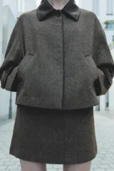 Minifalda gris con estampado de espiga, tiro alto, trabilla combinada a contraste y botón en delantero. Cierre lateral con cremallera oculta en costura.