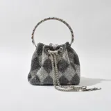 Cartera tipo bucket bag con cuerpo cubierto de strass en tonos grises y negros. Tiene asa rígida circular con incrustaciones de strass y cierre superior con cordón de ajuste y cadena decorativa.