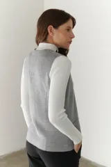 Chaleco gris de tejido de punto con cuello en V, cierre frontal con botones y bolsillos delanteros.