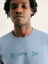 Camiseta blanca de algodón con cuello redondo y mangas cortas. Estampa rectangular con borde negro que contiene la frase "NATURAL ATMOSPHERE" en letras mayúsculas y una imagen de montañas y mar.