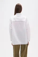 Camisa de algodón blanca, de corte ancho, con botones de madera y detalles de encaje calado en el frente, mangas y ruedo. Tiene cuello camisero y manga larga.