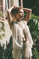 Blusa sin mangas color blanco con cuello alto, bordados y puntillas combinadas a tono, y apliques de abalorios. Cierre frontal con abertura, lazada y botón.