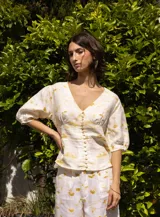 Camisa blanca con estampado floral amarillo, corte a la cintura, escote en V, manga abullonada 3/4 con elástico en puños y abotonadura central.