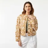 Chaqueta corta acolchada color beige con estampado abstracto en blanco, cuello redondo y cierre frontal con botones.