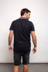 Chomba blanca de piqué con cuello polo y mangas cortas con ribete azul marino y negro. Cierre frontal con botones.