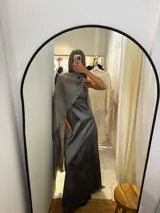 Vestido largo de tafeta con brillo, color gris o plateado, con escote asimétrico de un solo hombro y una pieza de seda liviana que cae como una capa o chal.