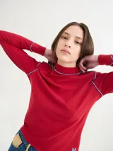 Polera negra de tela rib con cuello alto y mangas largas. Presenta pespuntes rojos en cuello, hombros y puños.