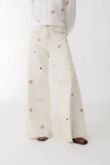 Pantalón de jean color crudo, corte wide leg, con bordados de cartas, dados y fichas de casino.